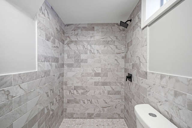 bathroom with toilet, tiled shower, and tile walls