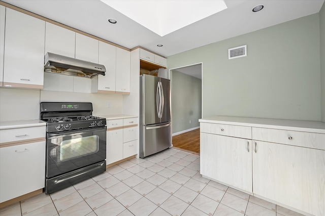 kitchen with white cabinets, stainless steel fridge, black gas range oven, and a skylight