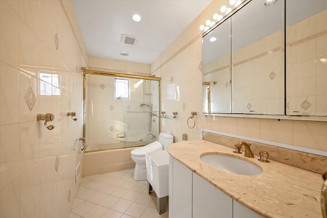 full bathroom with tile patterned floors, tile walls, combined bath / shower with glass door, toilet, and vanity