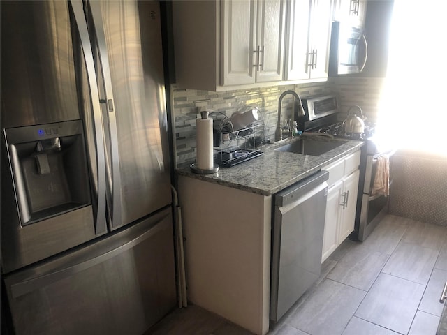 kitchen with sink, stone counters, appliances with stainless steel finishes, white cabinets, and decorative backsplash