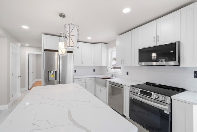 kitchen with appliances with stainless steel finishes, sink, white cabinets, hanging light fixtures, and light stone counters