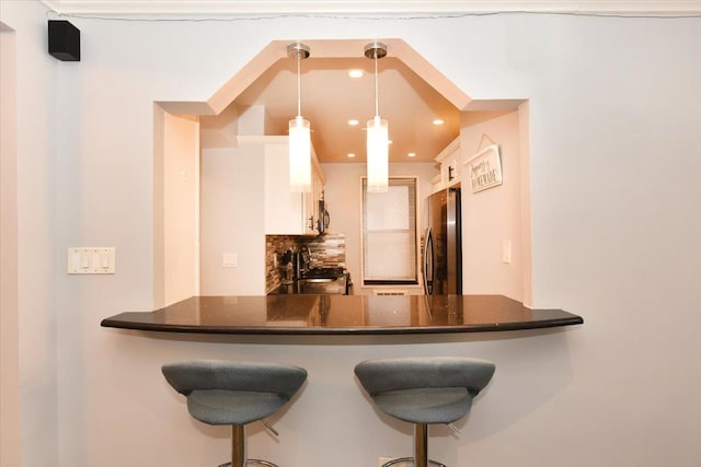 kitchen with a breakfast bar area, white cabinetry, hanging light fixtures, stainless steel appliances, and kitchen peninsula