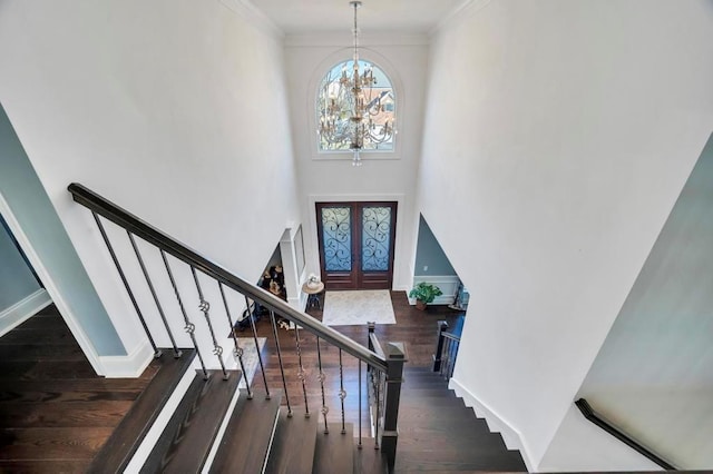 foyer entrance featuring crown molding, a towering ceiling, dark hardwood / wood-style floors, french doors, and a chandelier