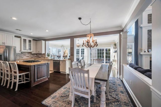 dining space with dark hardwood / wood-style floors, decorative columns, sink, crown molding, and an inviting chandelier