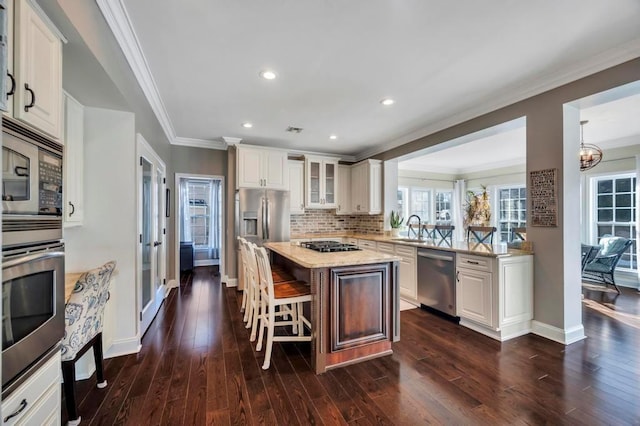 kitchen with sink, white cabinetry, stainless steel appliances, light stone counters, and a kitchen island