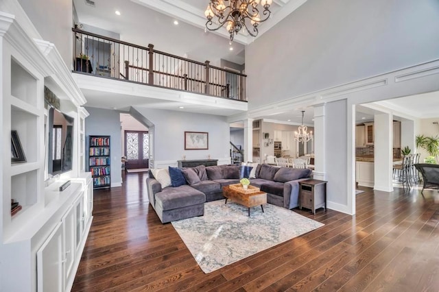 living room featuring decorative columns, dark hardwood / wood-style flooring, a high ceiling, and an inviting chandelier