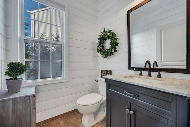 bathroom with toilet, vanity, wooden walls, and tile patterned flooring