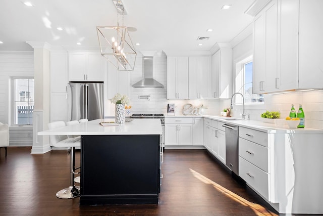 kitchen with sink, white cabinetry, a center island, wall chimney range hood, and stainless steel appliances