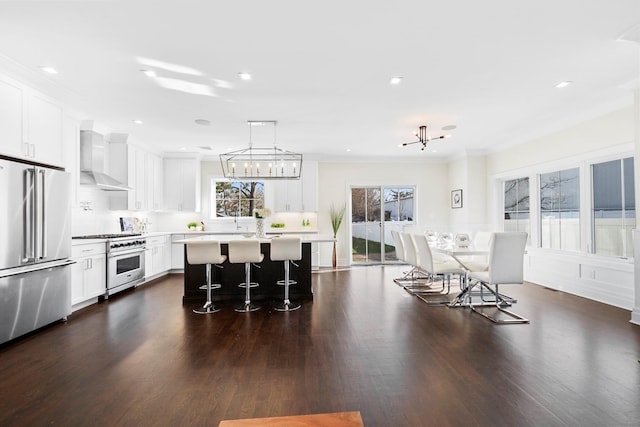 kitchen featuring a kitchen bar, high end appliances, wall chimney range hood, a kitchen island, and pendant lighting