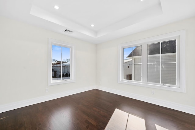 empty room with a tray ceiling and dark hardwood / wood-style flooring