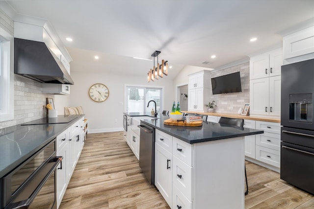 kitchen featuring white cabinetry, black appliances, custom range hood, and a center island with sink