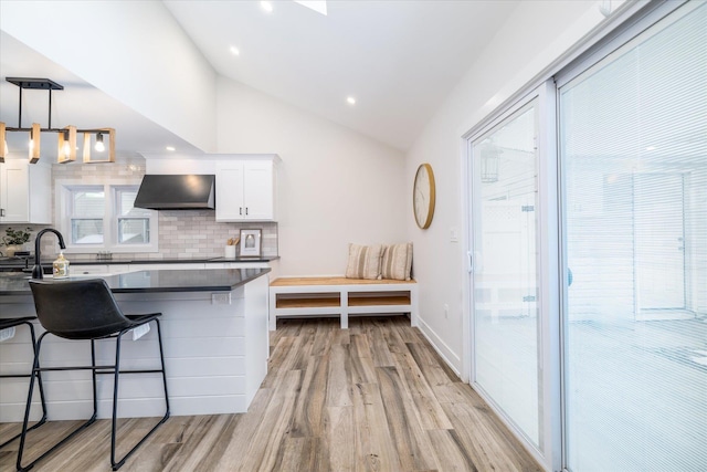 kitchen featuring vaulted ceiling, decorative light fixtures, white cabinetry, exhaust hood, and a breakfast bar