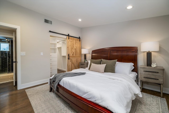 bedroom with a closet, a barn door, a spacious closet, and dark hardwood / wood-style flooring