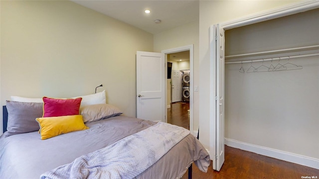 bedroom with dark hardwood / wood-style floors, stacked washer / drying machine, and a closet