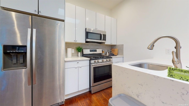 kitchen with appliances with stainless steel finishes, sink, backsplash, white cabinets, and dark wood-type flooring