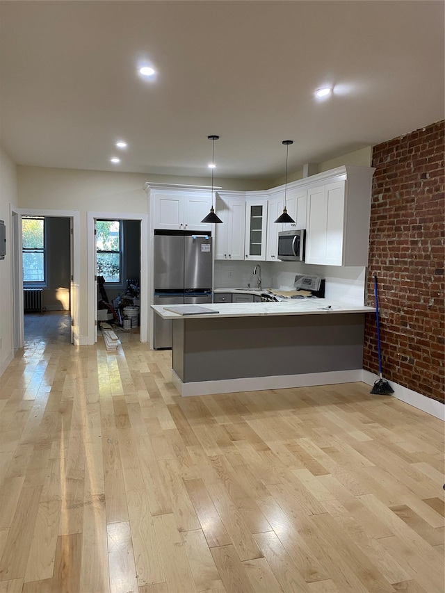 kitchen featuring kitchen peninsula, decorative light fixtures, white cabinetry, brick wall, and stainless steel appliances