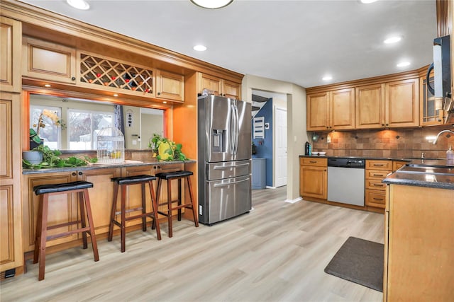 kitchen with appliances with stainless steel finishes, decorative backsplash, a kitchen breakfast bar, sink, and light hardwood / wood-style flooring