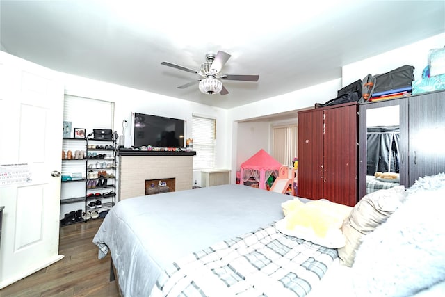 bedroom featuring dark hardwood / wood-style flooring, a brick fireplace, ceiling fan, and a closet