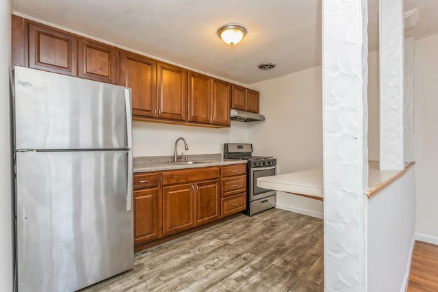 kitchen with sink, light hardwood / wood-style flooring, stainless steel appliances, and a textured ceiling