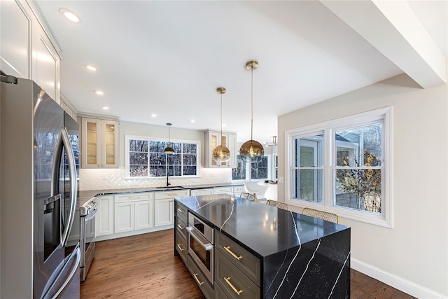 kitchen featuring hanging light fixtures, appliances with stainless steel finishes, backsplash, white cabinets, and a center island