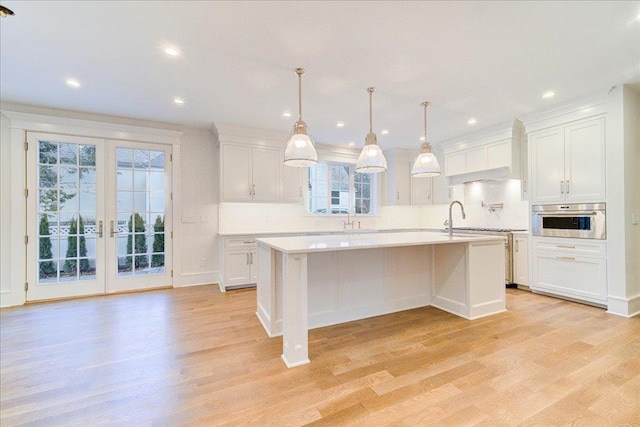 kitchen with a center island with sink, stainless steel oven, white cabinets, and light countertops