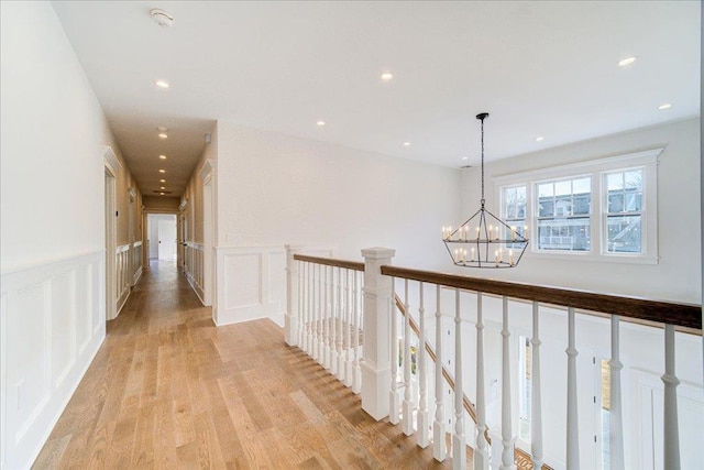 corridor with a wainscoted wall, a decorative wall, an inviting chandelier, an upstairs landing, and light wood-type flooring