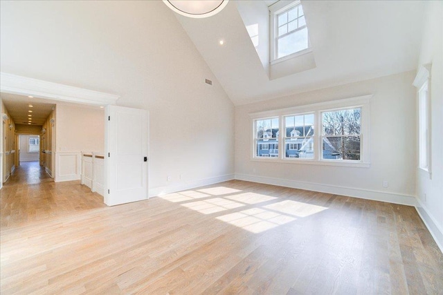 spare room with a healthy amount of sunlight, light wood-style floors, baseboards, and high vaulted ceiling