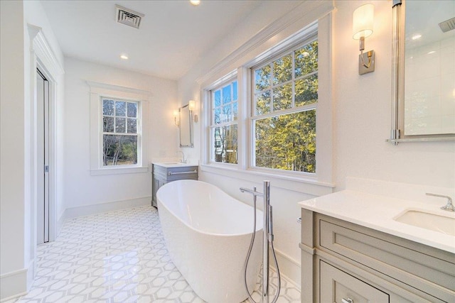 bathroom with a freestanding tub, recessed lighting, two vanities, a sink, and visible vents