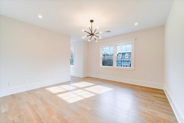 spare room with light wood-type flooring, an inviting chandelier, baseboards, and visible vents