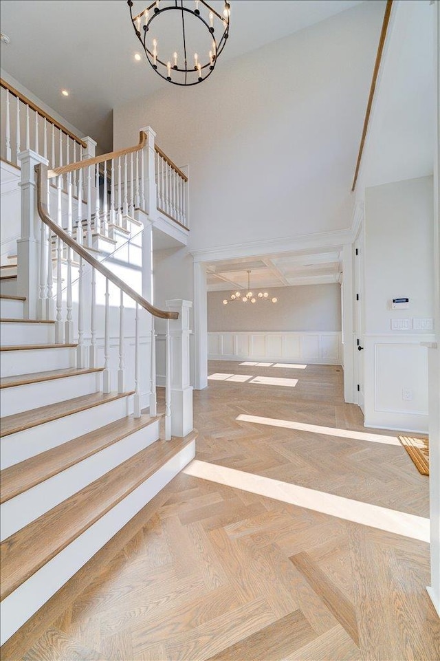 interior space with wainscoting, stairway, an inviting chandelier, a high ceiling, and a decorative wall