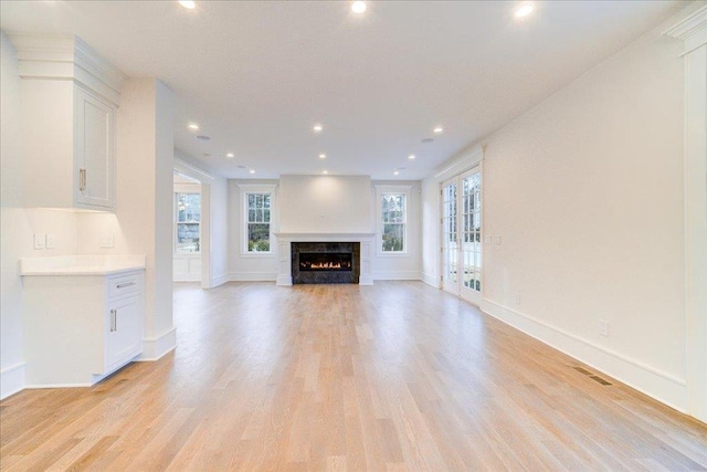 unfurnished living room featuring recessed lighting, visible vents, light wood-type flooring, a warm lit fireplace, and baseboards