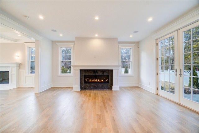 unfurnished living room with french doors, recessed lighting, light wood-style floors, a high end fireplace, and baseboards