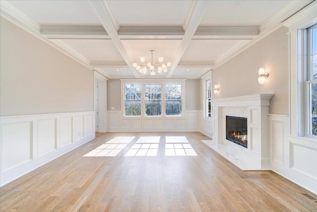 unfurnished living room featuring a high end fireplace, a notable chandelier, a decorative wall, and beamed ceiling