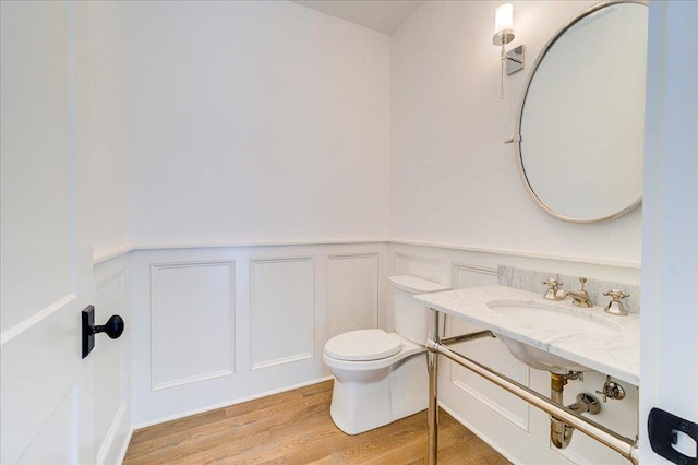 half bath featuring toilet, vanity, wood finished floors, and wainscoting