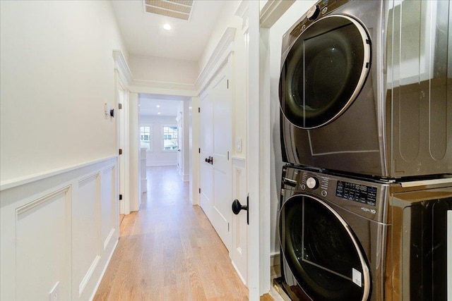 clothes washing area with light wood-style flooring, a decorative wall, laundry area, visible vents, and stacked washing maching and dryer