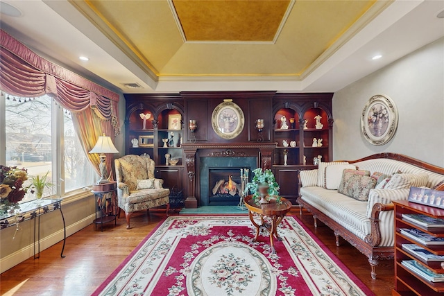 living area with crown molding, hardwood / wood-style flooring, and a raised ceiling