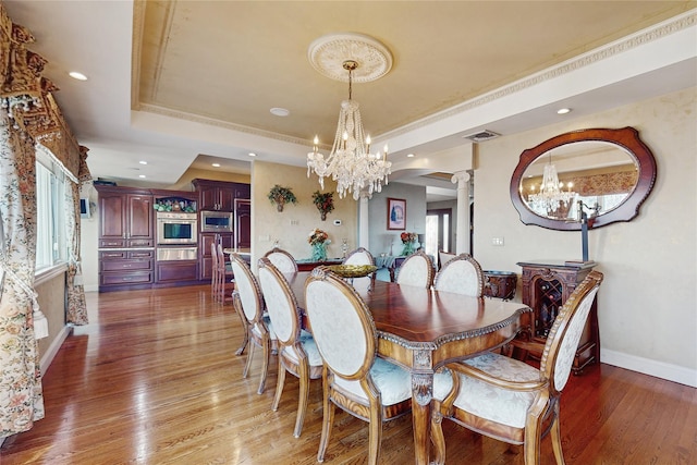 dining space featuring ornate columns, ornamental molding, a raised ceiling, dark wood-type flooring, and an inviting chandelier