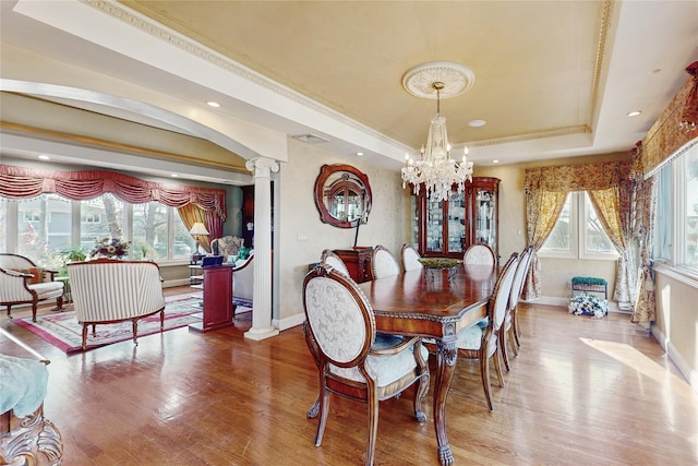 dining room with an inviting chandelier, plenty of natural light, a tray ceiling, and ornate columns