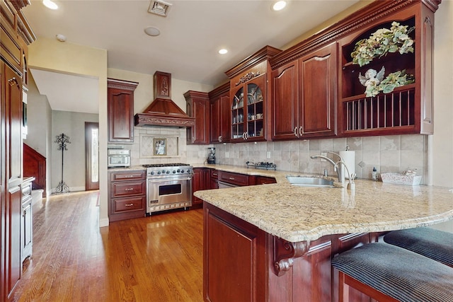 kitchen with luxury range, sink, kitchen peninsula, custom range hood, and decorative backsplash