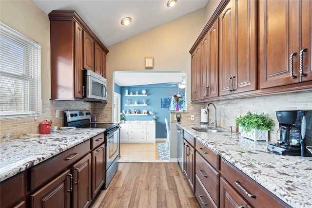 kitchen with light stone countertops, appliances with stainless steel finishes, lofted ceiling, light hardwood / wood-style floors, and sink