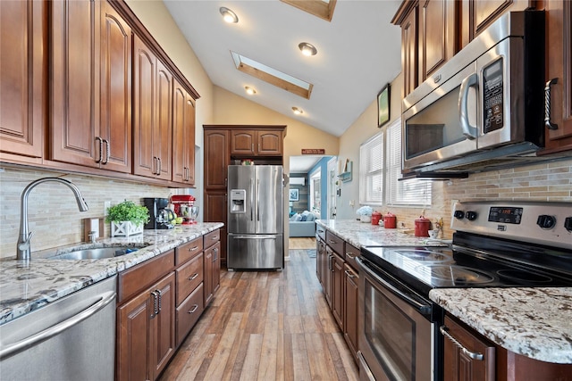 kitchen with light hardwood / wood-style floors, light stone countertops, appliances with stainless steel finishes, sink, and lofted ceiling with skylight