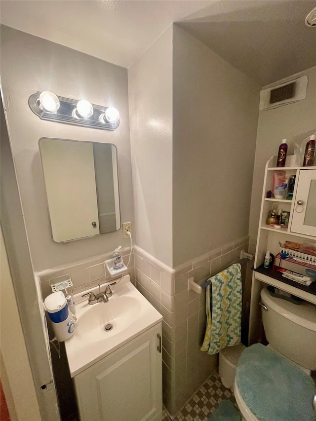 half bathroom with vanity, tile walls, toilet, and wainscoting