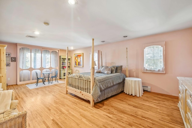 bedroom featuring multiple windows, a baseboard heating unit, and light hardwood / wood-style flooring