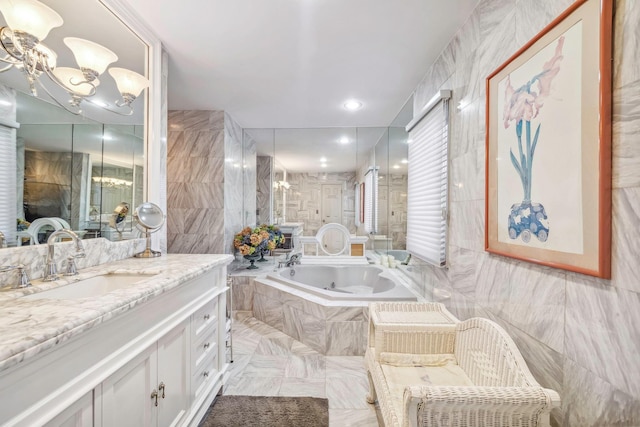 bathroom with tile walls, tiled tub, vanity, and a chandelier