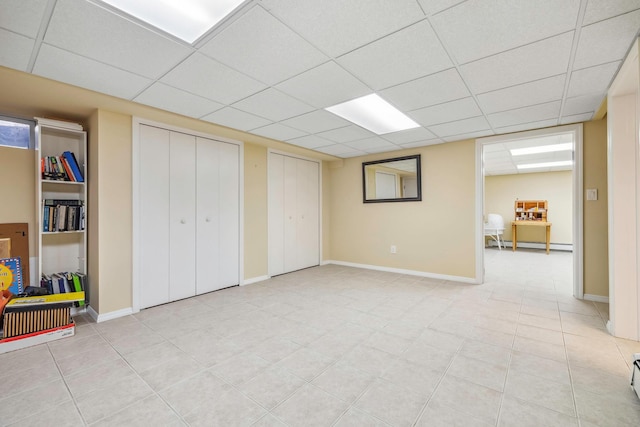 basement featuring a paneled ceiling and baseboard heating