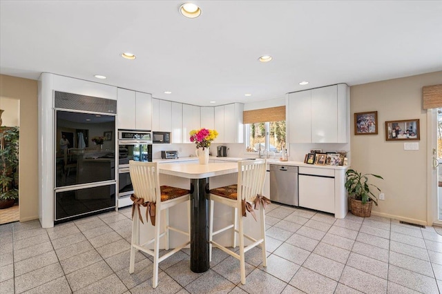 kitchen with a breakfast bar area, black appliances, white cabinets, and a kitchen island