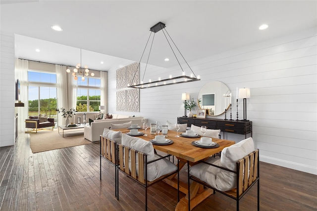 dining room featuring dark wood-type flooring, wooden walls, and an inviting chandelier