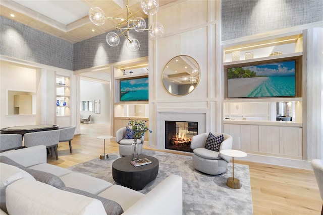 living room featuring hardwood / wood-style flooring, a high ceiling, a fireplace, built in shelves, and a notable chandelier