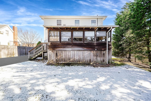 snow covered rear of property with a sunroom