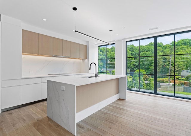 kitchen with an island with sink, sink, pendant lighting, and a wall of windows